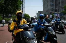 Food delivery workers on their vehicles on a street in Beijing