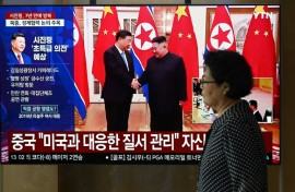 A woman walks past a television screen in Seoul Monday showing a news broadcast with file footage of the 2019 meeting between China's President Xi Jinping and North Korean leader Kim Jong Un