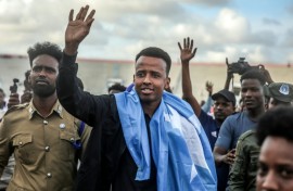 Somali referee Omar Artan waves to supporters while draped in the Somali flag as he is welcomed after returning to Mogadishu after being denied entry to the United States for the World Cup