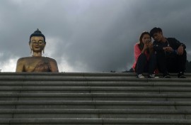 People look at a phone as they sit beside the Buddha Dordenma statue in Bhutan's capital Thimphu on August 25, 2018