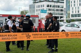 Damaged windows can be seen in the distance as police gather near the scene of a shooting in Montreal, which left three people dead