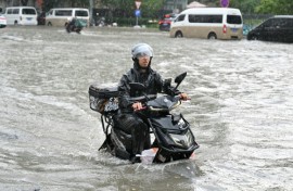 A man on a scooter makes his way along a flooded street in Beijing