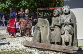 Sumbanese women wearing local ikat fabrics pass some of the statues and tombs that dot every village