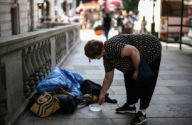 A woman puts some coins in a dish next to a man wrapped up with his dog on a London street