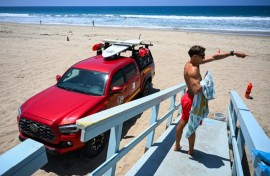 Los Angeles County lifeguard Maximus Oberto gestures as he monitors swimmers in the Pacific Ocean in Manhattan Beach