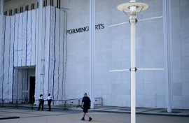 A person walks past scaffolding and a large protective tarp covering the facade of the John F. Kennedy Center for the Performing Arts