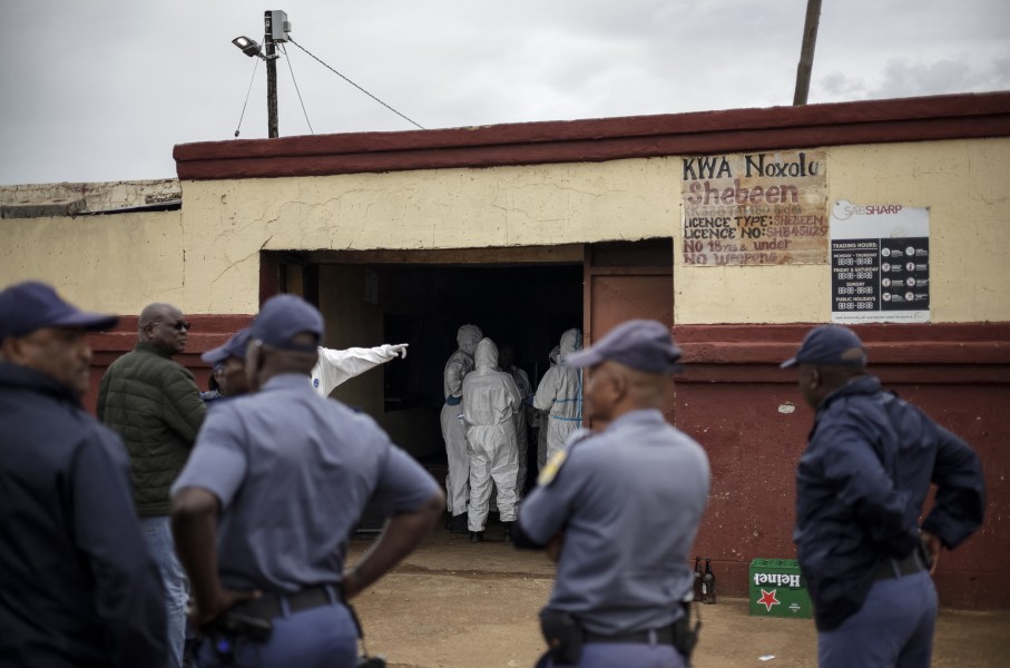 Police officers watch as SAPS Forensic Pathology Services members work at the scene of the Bekkersdal tavern attack. AFP/Emmanuel Croset