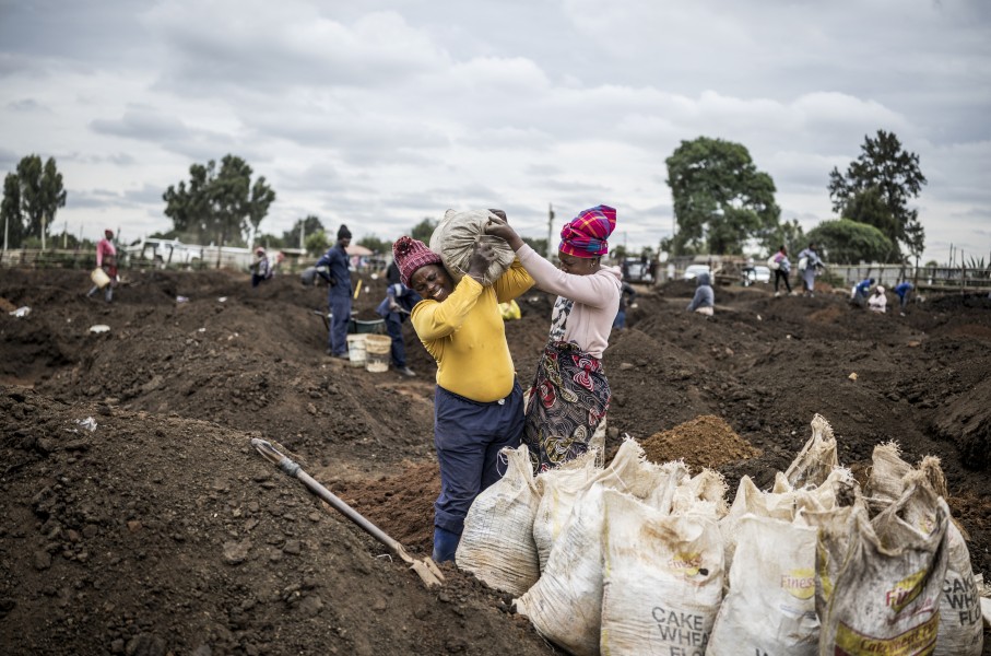 A woman grimaces as she is helped to load a sack of soil on her shoulder in a patch of land where artisanal miners look for gold outside Springs, Ekurhuleni, on February 15, 2026.