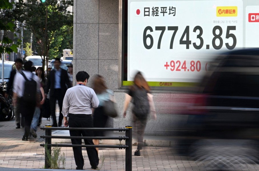 Pedestrians pass by a stock price indicator flashing its closing rate. AFP/Toshifumi Kitamura