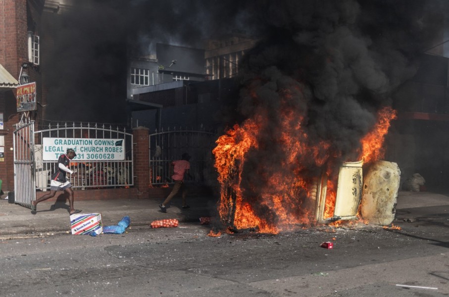 Protesters take cover past a burning car after clashes erupted between protesters and foreign nationals in Durban on October 8, 2026.