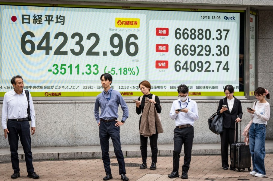 People wait to cross a street in front of an electronic quotation board displaying the Nikkei Stock Average on the Tokyo Stock Exchange. AFP/Yuichi Yamazaki