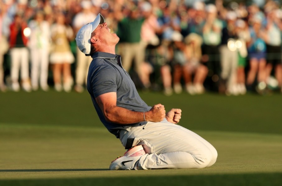 Rory McIlroy celebrates winning the 2025 Masters after falling to his knees on the 18th green having just completed a career grand slam