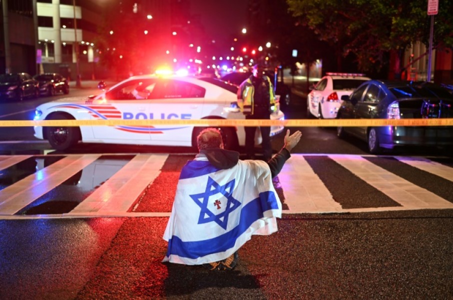 A man draped in the Israeli flag, bearing a cross and the name 'Jesus' at its center, gestures as Metropolitan Police officers secure the area outside the Capital Jewish Museum