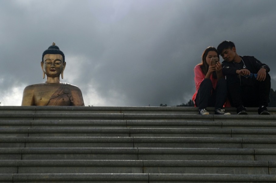 People look at a phone as they sit beside the Buddha Dordenma statue in Bhutan's capital Thimphu on August 25, 2018