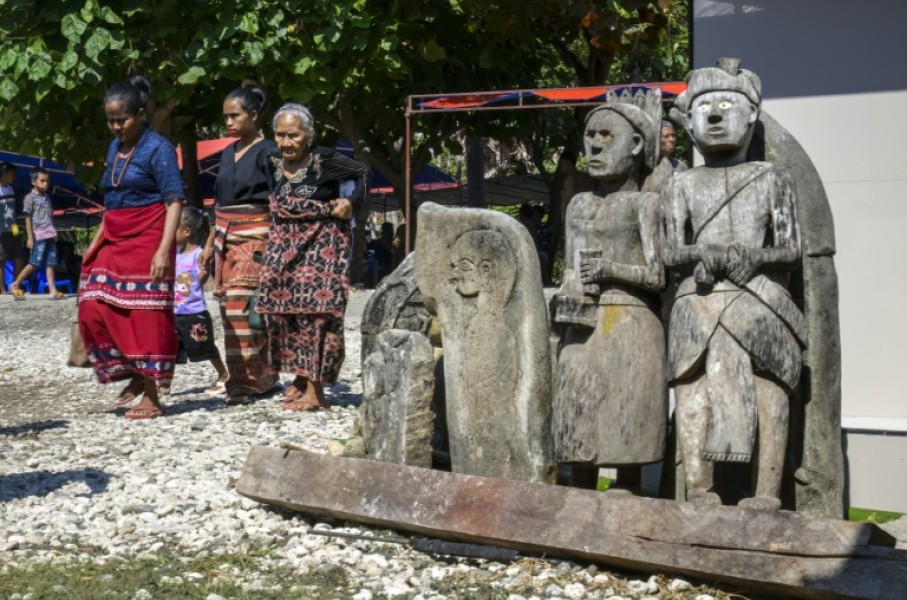 Sumbanese women wearing local ikat fabrics pass some of the statues and tombs that dot every village