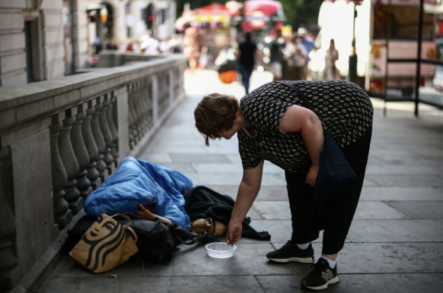 A woman puts some coins in a dish next to a man wrapped up with his dog on a London street