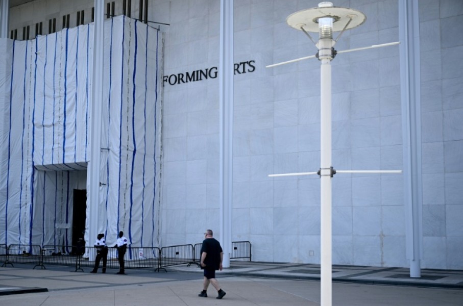A person walks past scaffolding and a large protective tarp covering the facade of the John F. Kennedy Center for the Performing Arts