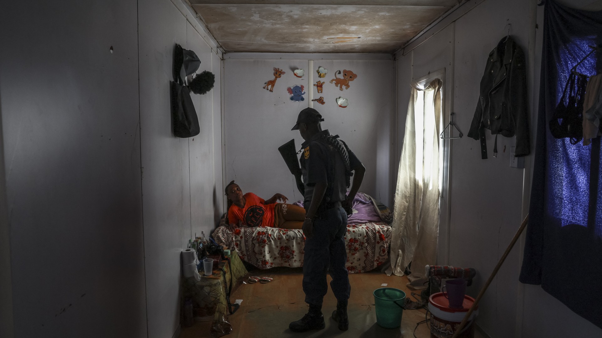 A hostel dweller lies on a bed while talking to a South African Police Service (SAPS) officer during a raid inside her home to retrieve looted goods during a protest at Diepkloof Hostel in Soweto on May 19, 2025.