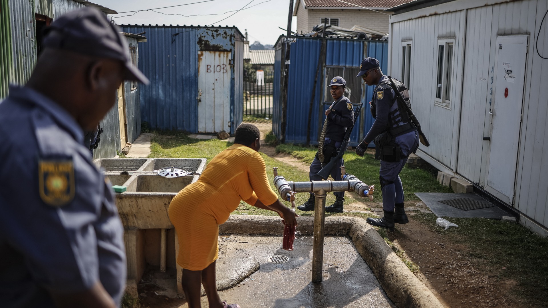 A hostel dweller speaks with South African Police Service (SAPS) officers walking past during a raid to retrieve looted goods during a protest at Diepkloof Hostel in Soweto on May 19, 2025.
