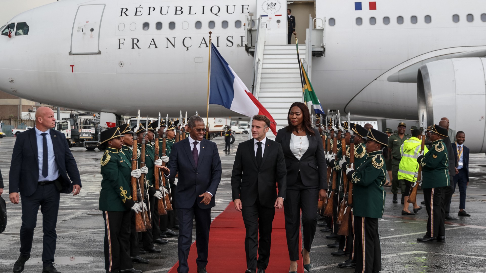France’s President Emmanuel Macron (C) is welcomed by South African Minister of the Department of Cooperative Governance and Traditional Affairs (COGTA) Velenkosini Hlabisa (CL) upon Macron's arrival at the OR Tambo International airport in Ekurhuleni on November 21, 2025 ahead of the G20 leader's Summit. (