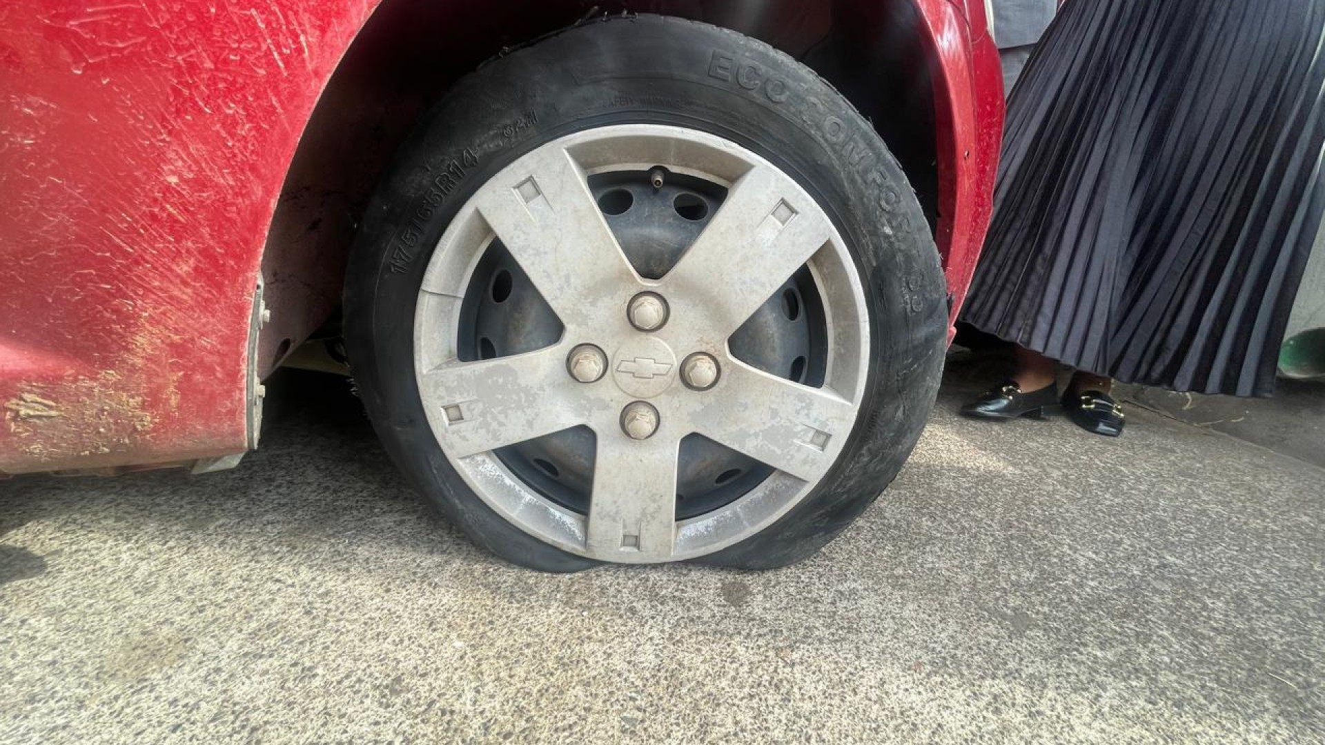 A red Chevrolet Aveo sedan, with a deflated tire.