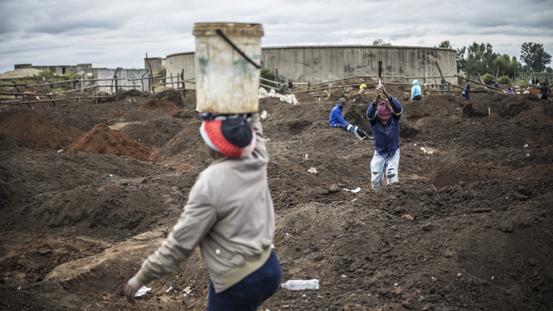 A woman balances a bucket full of soil as artisanal miners digging holes look for gold in a patch of land outside Springs, Ekurhuleni, on February 15, 2026.