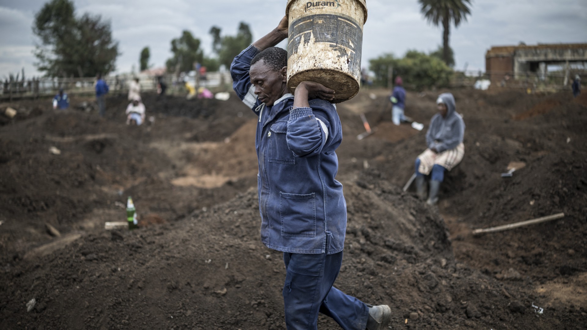 A man carries a bucket full of soil as artisanal miners digging holes look for gold in a patch of land outside Springs, Ekurhuleni, on February 15, 2026.