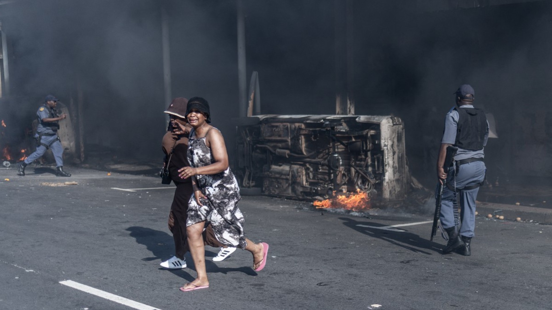 Members of the South African Police Service (SAPS) assist residents to take cover after clashes erupt between protesters and foreign nationals in Durban on October 8, 2026.
