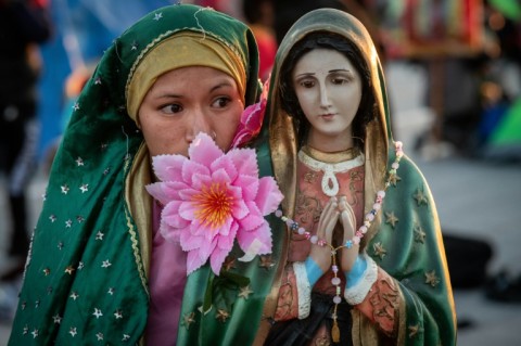 A woman stands next to an image of the Virgin of Guadalupe outside the Guadalupe basilica in Mexico, December 12 2022