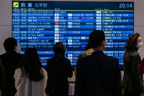 People wait in front of a board showing international flight arrivals at Tokyo's Haneda international airport 
