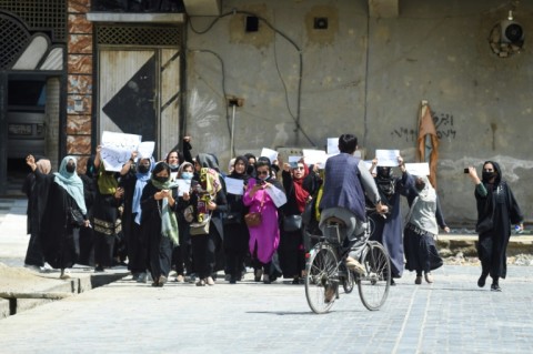 Afghan burqa-clad women walk past a Taliban security personnel along a street in Jalalabad, Afghanistan