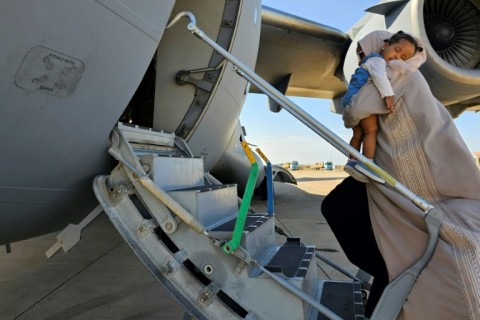 An evacuee holding a sleeping toddler boards an Abu Dhabi-bound plane at Port Sudan airport