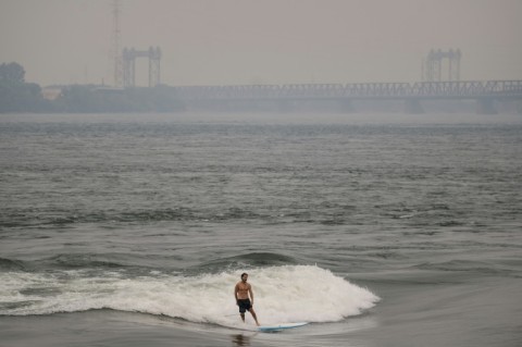 A man surfs in the St. Lawrence river with smoke caused by wildfires in northern Quebec in the background in Montreal, Canada on June 25, 2023