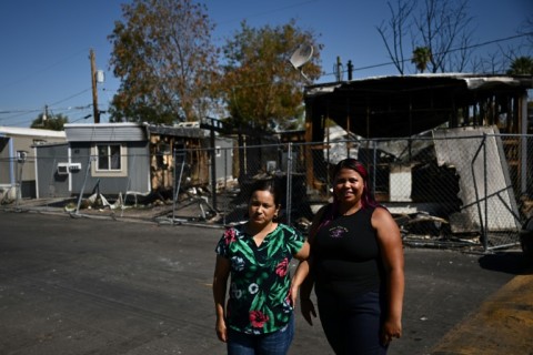 Rosalia Licea (L) and neighbor Wendy Salinas pose on July 20, 2023 near the remains of a neighboring mobile home recently destroyed in a fire, during a record heat wave in Phoenix, Arizona