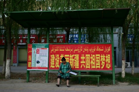 A woman sits at a bus stop bearing a Chinese government slogan in Yarkant, Xinjiang