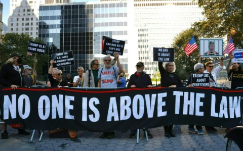 Protestors hold banners outside New York State Supreme Court ahead of the start of a civil fraud trial against Donald Trump