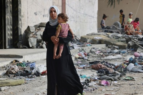 A Palestinian woman carries a child as she walks through debris in Gaza's residential neighbourhood of Rafah, following Israeli airstrikes on the southern Gaza Strip 