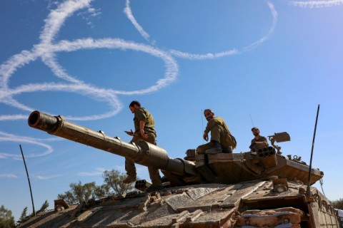 Israeli troops gather stand atop a tank on the border with the Gaza Strip