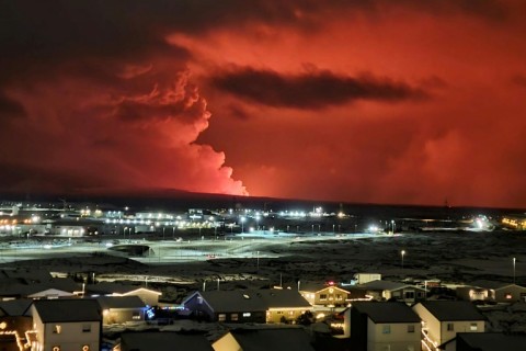 Houses in Iceland's Hafnarfjordur are seen as smoke billows in the distance, the night sky turned orange by lava