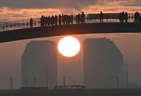 People watch the first sunrise of the new year from a footbridge overlooking the city skyline in Seoul on January 1, 2024