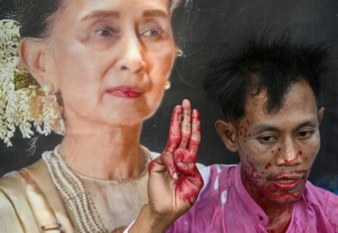 A protester covered in fake blood flashes a three-finger salute next to an image of detained civilian leader Aung San Suu Kyi during a demonstration outside the UN office in Bangkok on February 1, 2024