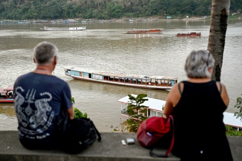 Tourists watch boats cruising on the Mekong river in Luang Prabang
