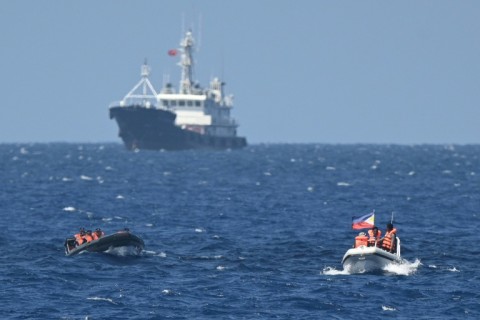 Chinese coast guard personnel aboard a rigid hull inflatable boat (front L) trail a Philippine vessel (front R) near the China-controlled Scarborough Shoal