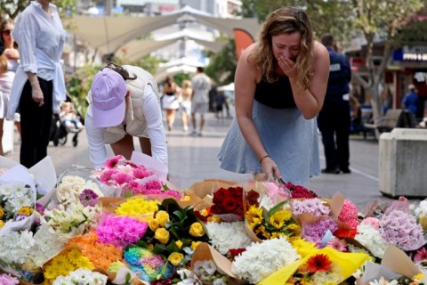 People react as they leave flowers outside the Westfield Bondi Junction shopping mall in Sydney on April 14, 2024