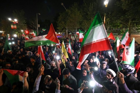 Demonstrators wave Iran's flag and Palestinian flags as they gather in front of the British Embassy in Tehran