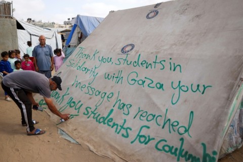 On a tent for displaced Palestinians in Rafah, a man writes a message of thanks to protesting students in the United States 