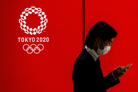 A masked man walks past a logo of the Tokyo 2020 Olympics 