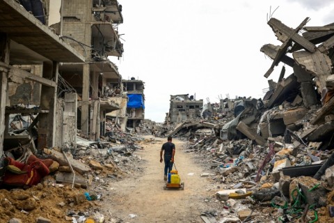 A man pulls water containers as he walks past destroyed buildings in Khan Yunis on May 5, 2024