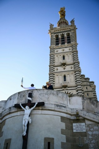 Basile Boli holds the Olympic torch aloft in front of the basilica of Notre-Dame de la Garde in Marseille