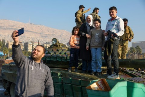 A man takes a selfie with his family standing atop a tank as they celebrate in Damascus